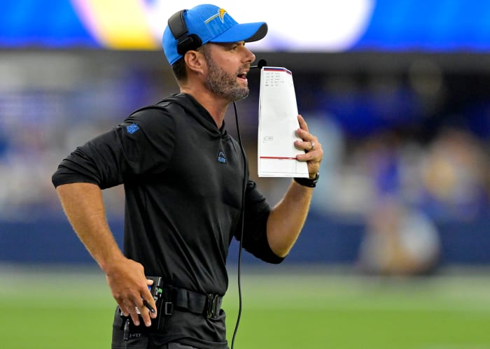 Brandon Staley talks into a headset on the sideline while holding a piece of paper up to cover his mouth